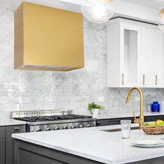 a kitchen with marble counter tops and gold hood over the stove top, surrounded by white cabinets