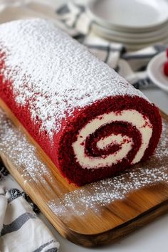 a red velvet roll covered in powdered sugar sits on a cutting board next to plates and utensils