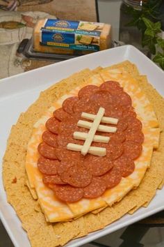 a football shaped appetizer on a plate with crackers, cheese and pepperoni