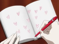 someone is writing on an open book with hearts drawn on it and holding a red pen