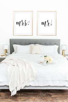 a white bed with two framed pictures above it and flowers on the end table next to it