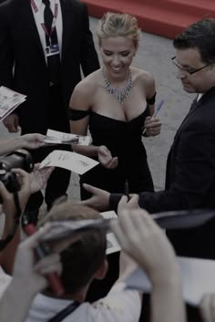 a woman in a black dress signing autographs for people at an event with cameras around her