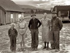 a group of people standing next to each other in front of a wooden building on a dirt field