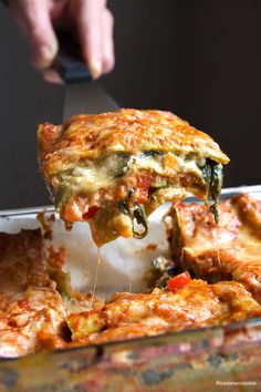 someone is taking a slice of lasagna casserole with cheese and spinach