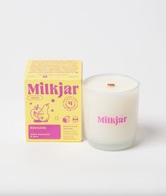 a white candle next to a box of milk on a white surface with pink writing