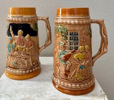 two beer mugs sitting on top of a white table next to eachother