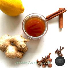 a cup of tea next to an orange, cinnamon and lemon on a white surface