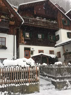 a house with snow on the roof and fence in front of it, surrounded by trees