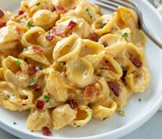 a white plate topped with macaroni and cheese covered in bacon next to a fork