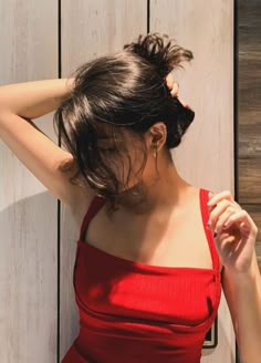 a woman in a red dress leaning against a wooden wall with her hand on her head