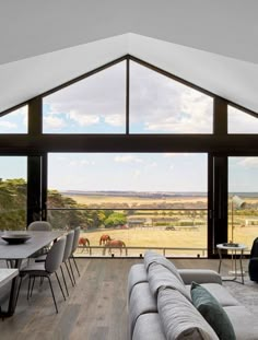 a living room filled with furniture next to a large glass window overlooking horses grazing on the field