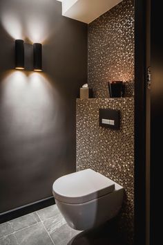 a modern bathroom with black and gold mosaic tiles on the walls, along with a white toilet