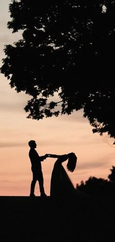 two people standing next to each other under a tree at sunset with the sky in the background