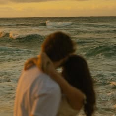 a man and woman embracing on the beach with waves crashing in the background at sunset