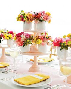 there are many flowers in the vases on this tiered cake stand that is decorated with yellow napkins and white plates