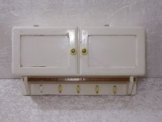 an old white wall mounted cabinet with two doors and three brass knobs on it