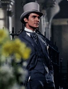 a man in a suit and top hat standing next to flowers