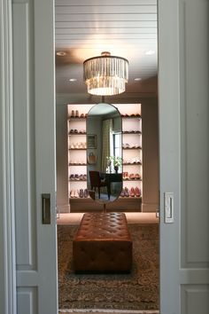 an entry way with a bench, mirror and chandelier in the background is a closet full of shoes