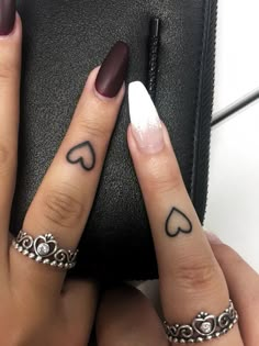 two fingers with hearts tattooed on them, one has a ring and the other has a heart