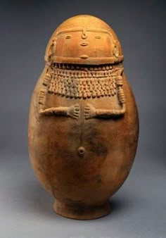 an old pottery vase with a face and head on the top, sitting in front of a gray background