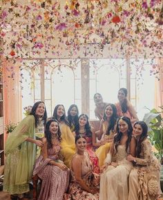 a group of women sitting next to each other in front of a flower covered ceiling