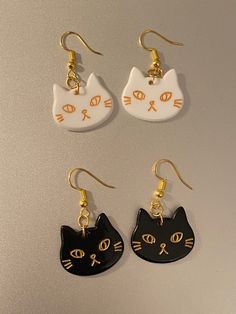 three pairs of earrings with cats painted on them, one is black and the other is white