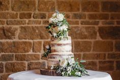 a wedding cake sitting on top of a table next to a brick wall with greenery