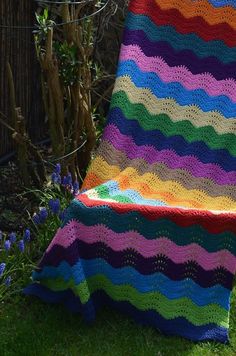 a multicolored crocheted blanket sitting on top of a wooden chair in the grass