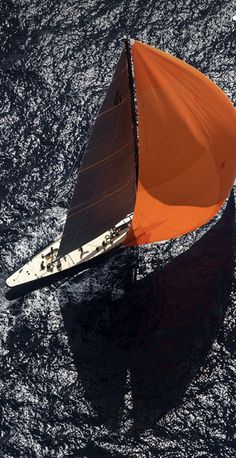 an orange sail boat floating on top of the ocean