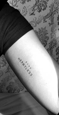 a woman with a tattoo on her arm that says,'heartless'in cursive writing