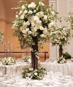 a tall centerpiece with white flowers and greenery sits on top of a round table