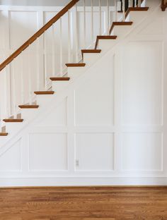 an empty room with white walls and wood floors, stairs leading up to the second floor