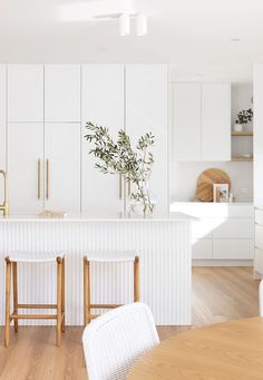 a kitchen with white cabinets and wooden flooring next to a dining room table filled with chairs