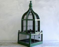 a green birdcage sitting on top of a white table next to a wall