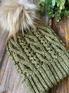 a knitted hat with a pom - pom sits on a wooden surface