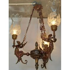 an antique chandelier hanging from the ceiling with two glass shades on it's arms