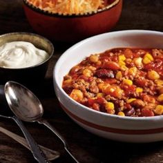 a bowl of chili with corn, cheese and sour cream next to it on a table