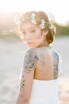 a woman with tattoos on her back standing in front of the sun wearing a white dress