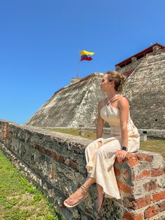 a woman sitting on top of a stone wall next to a yellow and red kite