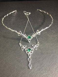 a silver bracelet with green stones on it's sides and an arrow charm hanging from the side