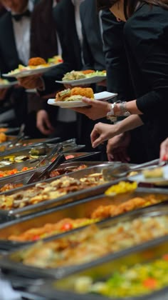 many people are serving themselves food at a buffet line up to get their plates off the table