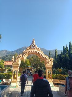 people are walking through an archway in the middle of a park with mountains in the background