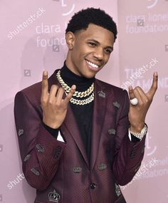 a man in a purple suit and black shirt making the v sign with his fingers