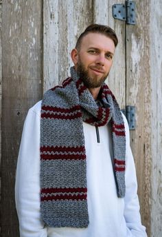 a man wearing a scarf standing in front of a wooden fence with his hands on his hips