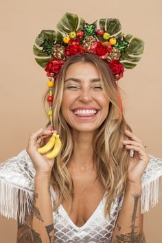 a woman wearing a flower crown and holding a banana in front of her face while smiling at the camera