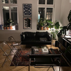 a living room with black leather furniture and lots of plants on the windows sill