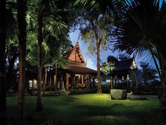 the house is surrounded by palm trees and other greenery at night, with lights on