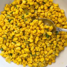 a white bowl filled with corn next to a spoon