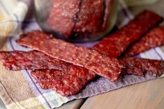 several pieces of meat sitting on top of a cloth next to a jar of pickles