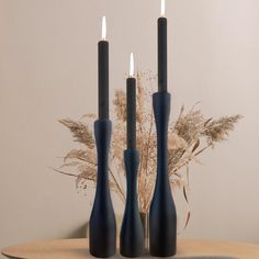 three black candles sitting on top of a wooden table next to flowers and dry grass